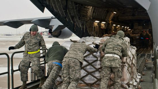 Men in army uniforms push cargo up into a plane