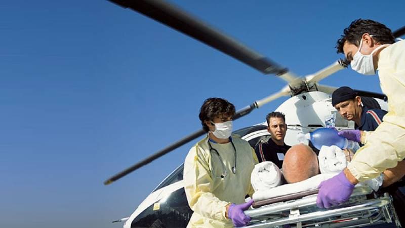A group of paramedics carry a patient on a stretcher off of a helicopter.
