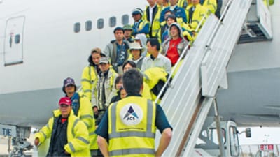 A group of passengers disembark from a plane with safety vests on.