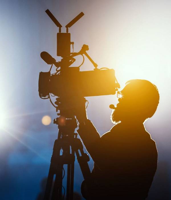 Silhouette of a man operating a camera with stage lights in the background.