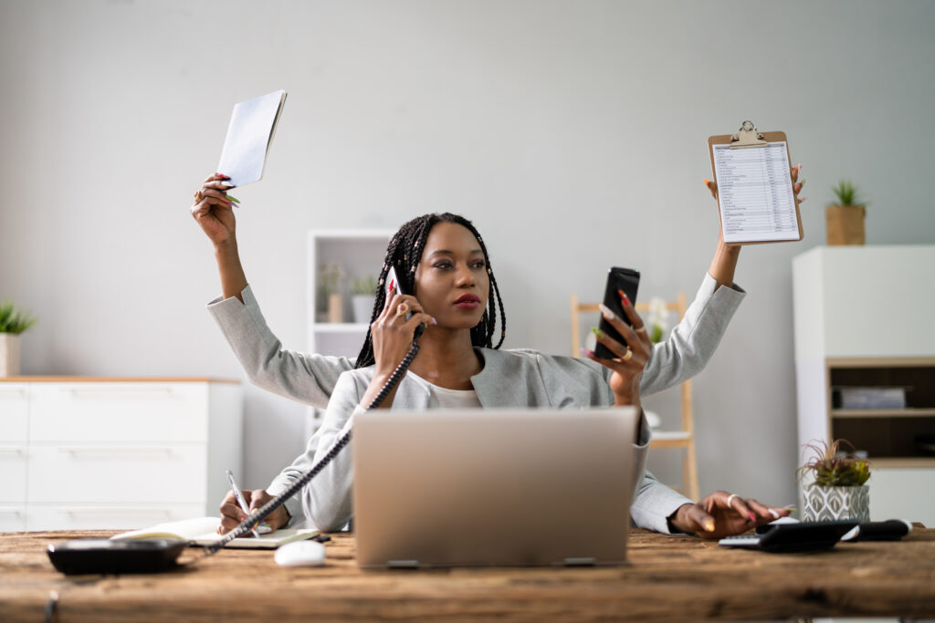 Multitasking businesswoman with many arms at desk in office.